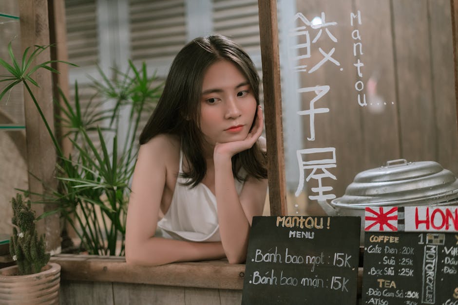 Young woman leaning on a food stall counter with Asian menu signs, looking thoughtful.