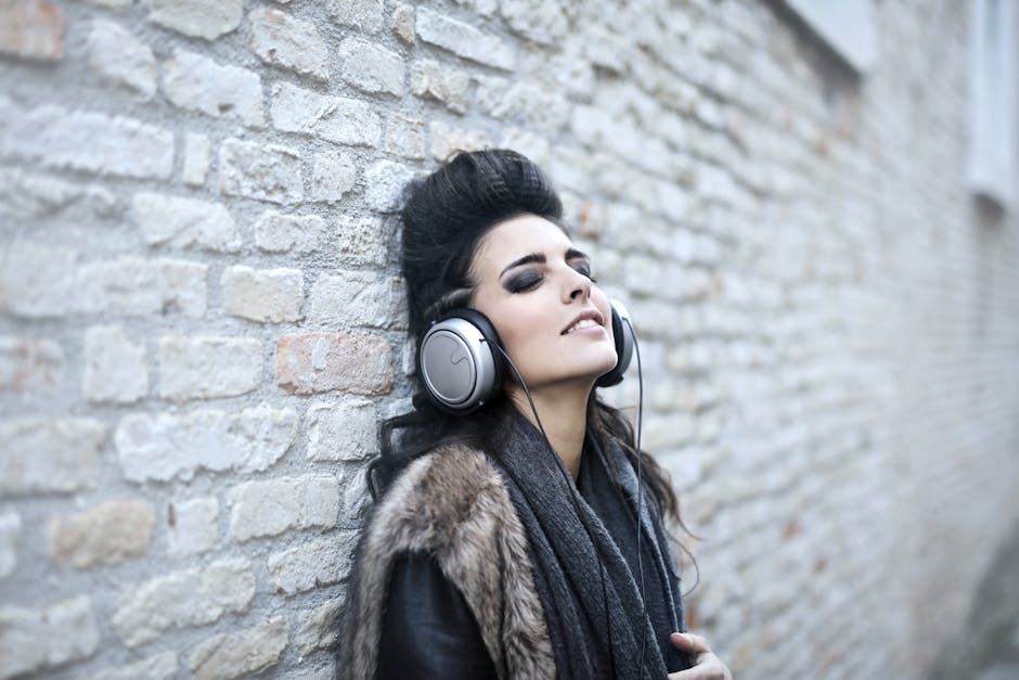 Stylish young woman leaning against a brick wall, enjoying music with headphones, eyes closed in relaxation.