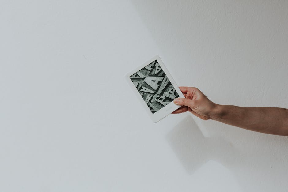 A minimalist photo of a hand holding a modern e-reader against a white background.