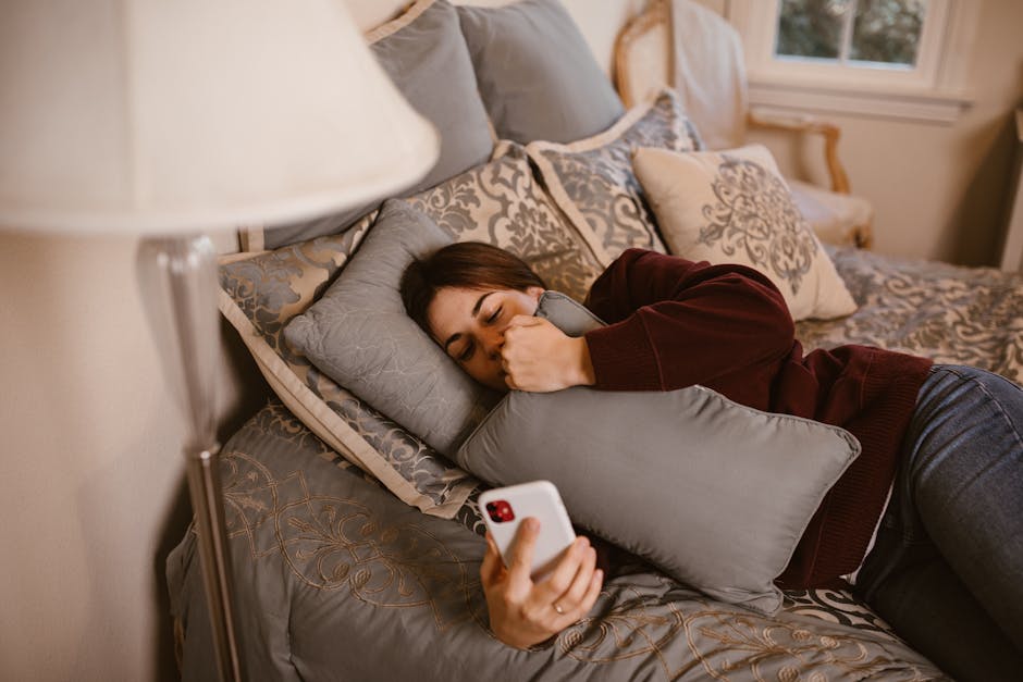 A young woman lying on a bed, holding a phone and a pillow, symbolizing relaxation and connection.