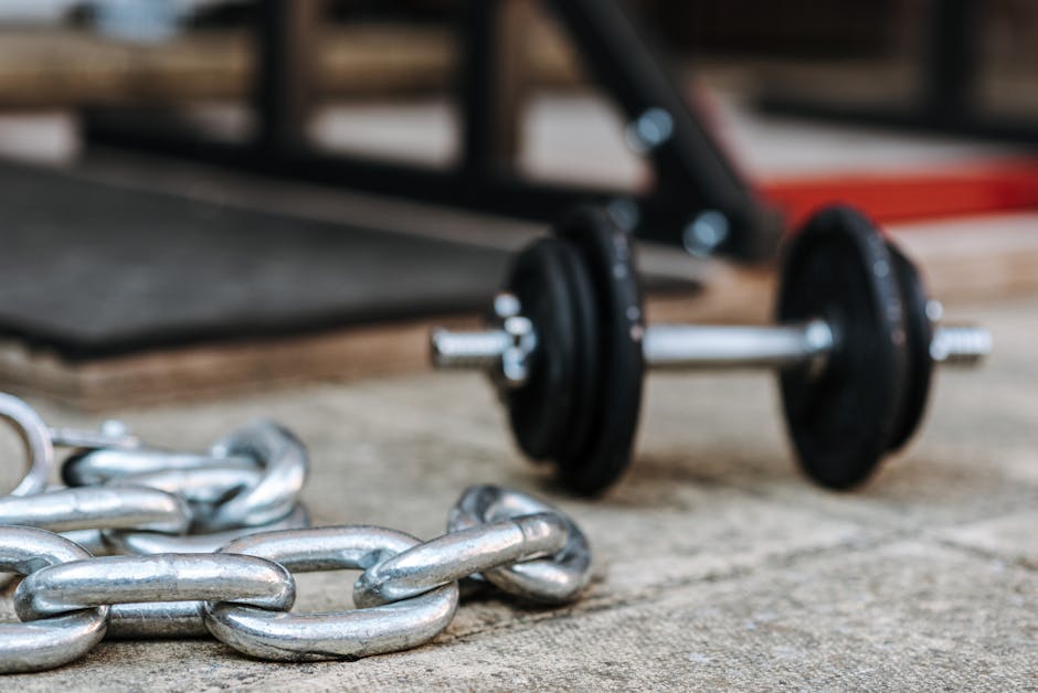 Close-up of a metal dumbbell and heavy chain on a gym floor, symbolizing strength and fitness.